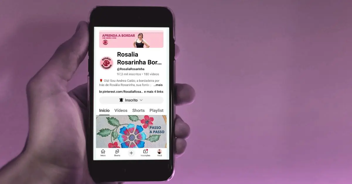 uma mão segurando um smartphone com a imagem da capa do canal de bordado livre “rosália rosarinha bordado” no youtube para ilustrar uma chamada do site agulhas da resistência subvertendo linhas e pontos sobre artesanato