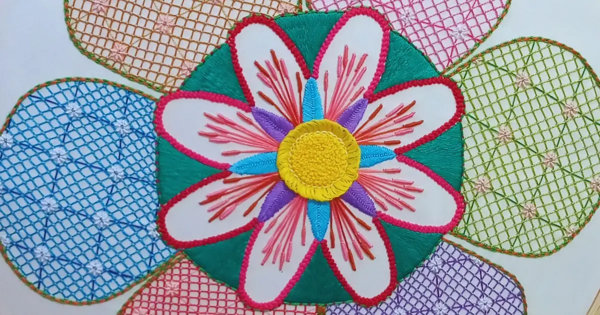 bordado grande de uma flor cheia de detalhes dentro de outra flor maior, com pétalas em padrão fantasia. peça da artesã andrea catão de rosália rosarinha e agulhas da resistência