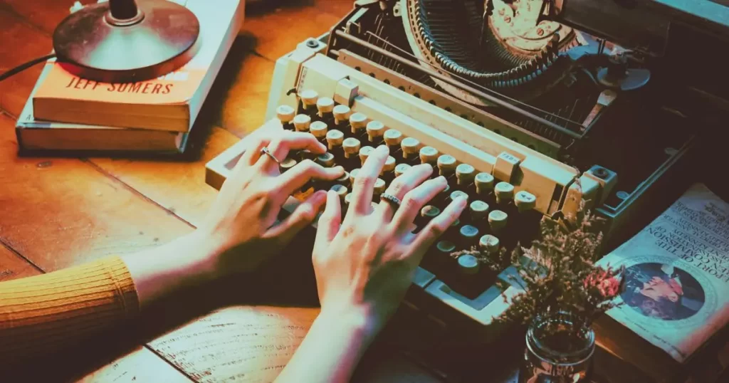 mãos sobre o teclado de uma máquina de escrever em cima de uma mesa, para evidenciar a necessidade de escrever. a imagem ilustra um texto no blog do site agulhas da resistência subvertendo linhas e pontos, cujo título é "escrever é mais do que ser lido"