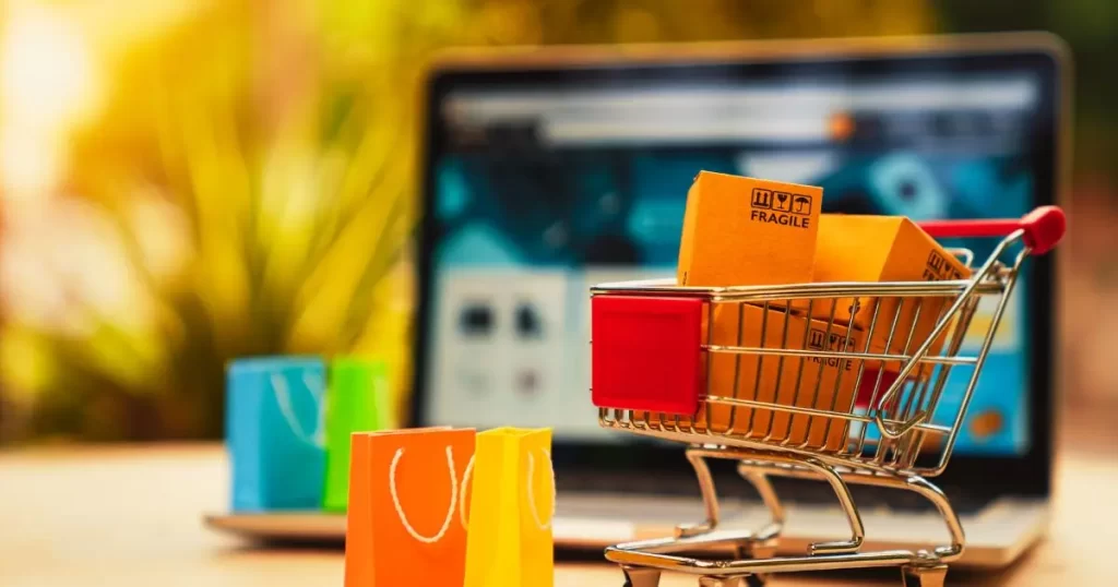 imagem de carrinho de compras com caixas e sacolas em frente ao computador para evidenciar que se trata de venda online, de compra online. A imagem ilustra uma chamada para a loja do site agulhas da resistência subvertendo linhas e pontos