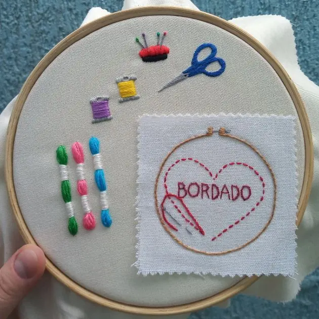 kit de bordado interna tela bordada em bastidor com desenho de linhas meadas, agulhas e alfinetes, tesoura e uma mini tela bordada com um coração escrito bordado. peça produzida pela artesã andrea catão de rosália rosarinha e agulhas da resistência