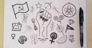 risco para bordar com vários símbolos da luta de classes, das mulheres por igualdade, comunismo, palestina livre, flores e material de bordado e crochê. são elementos que representam os valores do site e projeto agulhas da resistência subvertendo linhas e pontos, de artesanato e política. embaixo do desenho um tecido de algodão para ser bordado e em cima uma caneta para passar o risco para o tecido