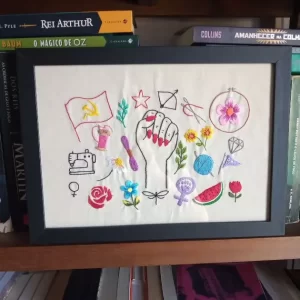 bordado em tecido de algodão emoldurado em madeira preta vertical com vários símbolos para o banner do site agulhas da resistência para a série manifesto bordado, criado e produzido pela artesã andrea catão. são bordados de desenhos de um punho feminino erguido, flores, folhas, como rosas e margarida, espelho de vênus, símbolo feminista, bandeira comunista, novelo de linha, carretel, agulhas, libélula, estrela etc