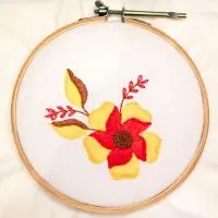 bordado à mão de flor dentro de uma moldura de bastidor de madeira, criado pela artesã Andrea Catão