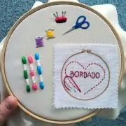 tela bordada em bastidor com desenho de kit para bordar, com linhas meadas, agulhas e alfinetes, tesoura e uma mini tela bordada com um coração escrito bordado. peça produzida pela artesã andrea catão de rosália rosarinha e agulhas da resistência