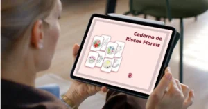 pessoa segurando um tablet com a capa do ebook "caderno de riscos florais - rosália rosarinha", com o título em destaque e riscos e bordados à mão