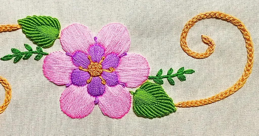 flor bordada à mão na cor rosa e lilás e folhas bordadas com ponto rococó e detalhes com ponto corrente húngara. bordado pela artesã andrea catão para o canal rosália rosarinha no youtube
