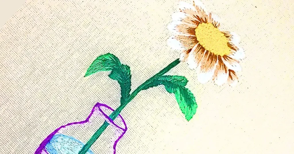 margarida em vaso bordada à mão em pintura de agulha. peça produzida pela artesã andrea catão para o canal rosália rosarinha bordado